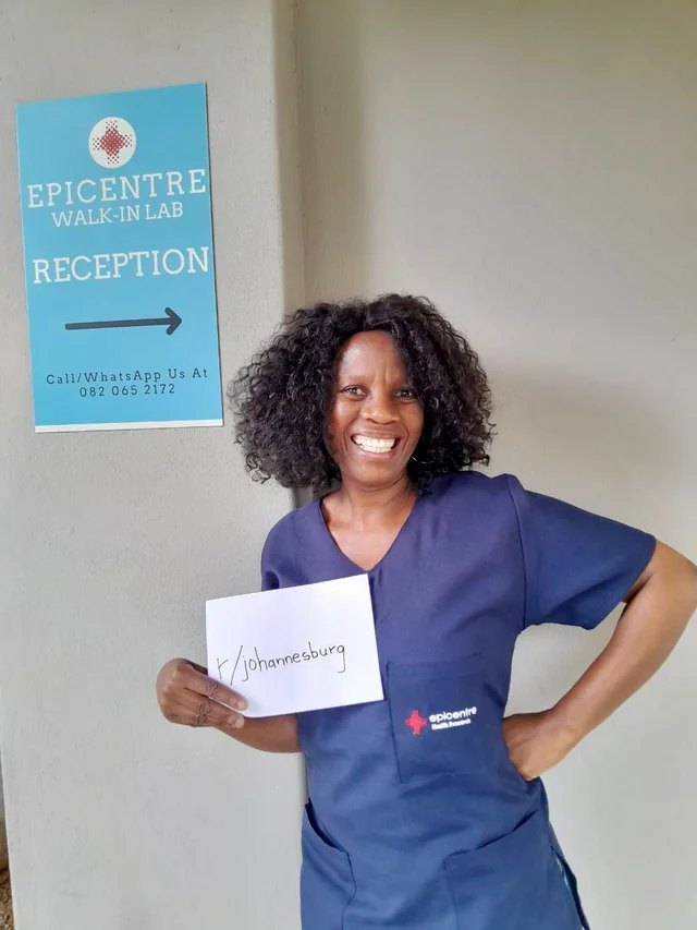 Sister Lucia, Registered Nurse, outside the Epicentre walk-in lab reception in Parktown North, holding a card reading r/johannesburg